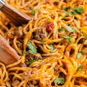 Cheesy taco spaghetti being lifted with tongs, showing ground beef, pasta, and melted cheese