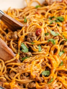 Cheesy taco spaghetti being lifted with tongs, showing ground beef, pasta, and melted cheese