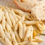 Creamy penne pasta on a plate with a slice of bread.