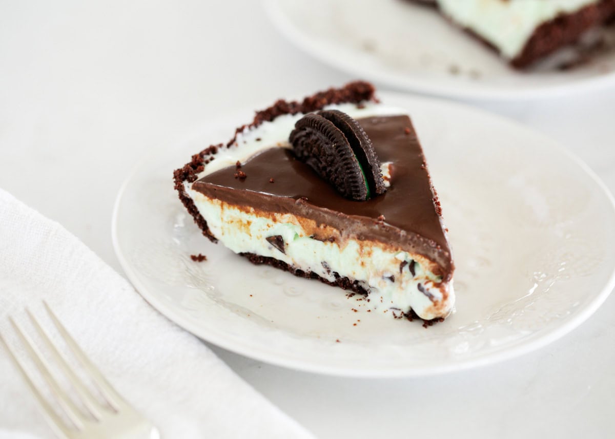 This 5-ingredient summer treat is a cool twist on classic grasshopper pie made with an Oreo crust, mint chocolate chip ice cream and topped with silky chocolate ganache. A slice of grasshopper pie with mint ice cream on a plate.