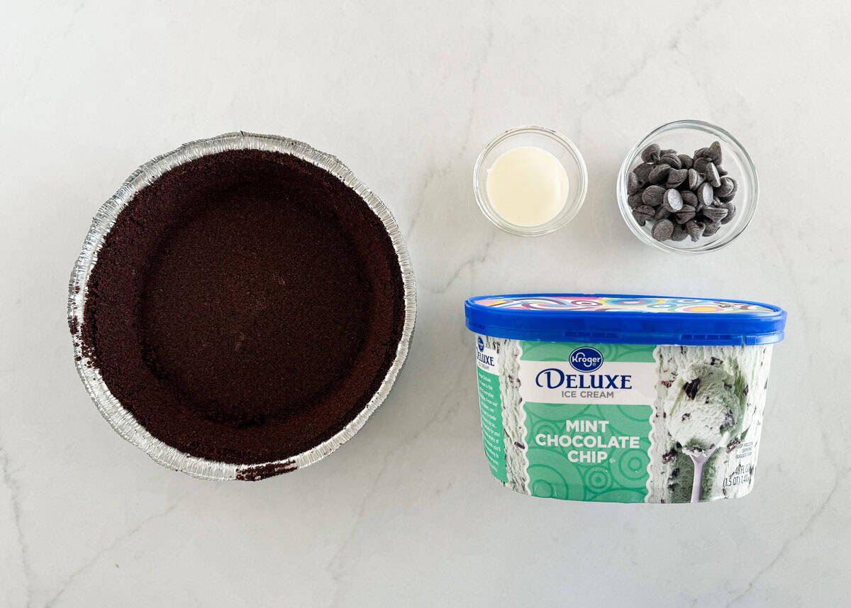 Oreo pie crust, mint ice cream, chocolate chips and heavy cream on the counter.