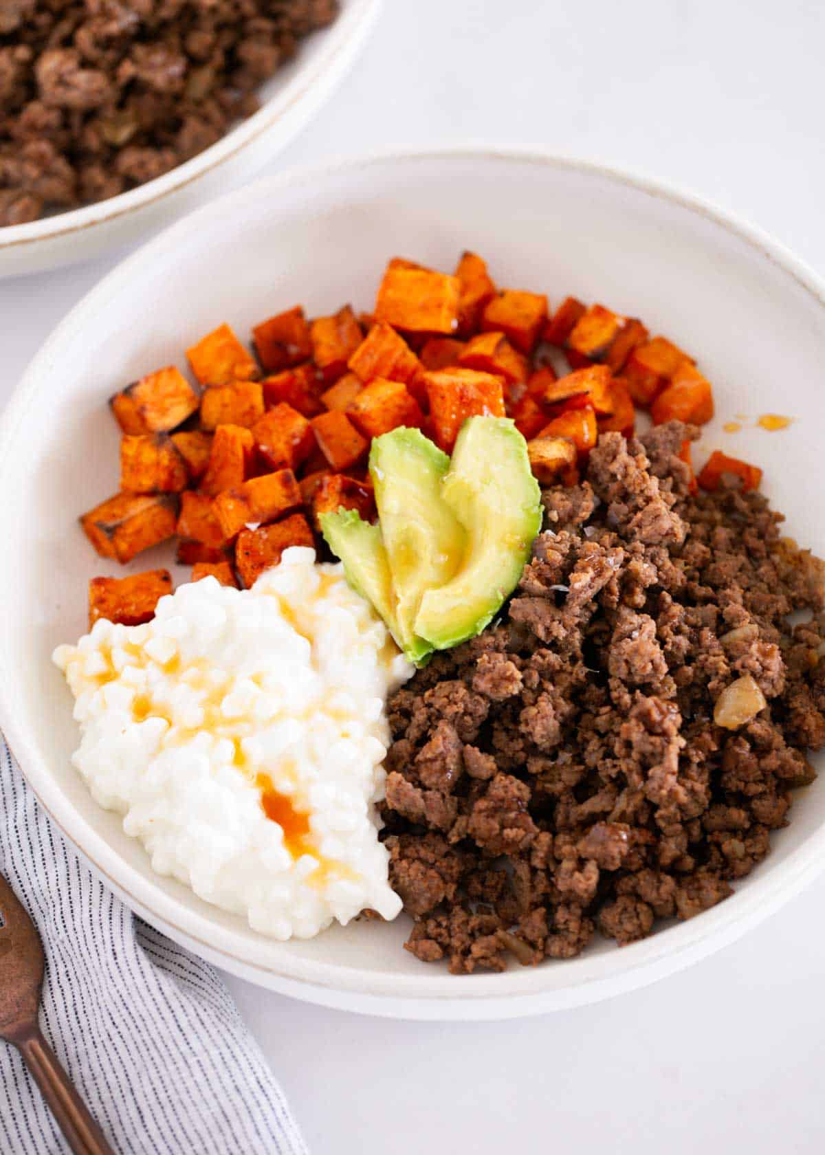 Assembled sweet potato cottage ground beef bowl with a drizzle of hot honey and avocado slices.