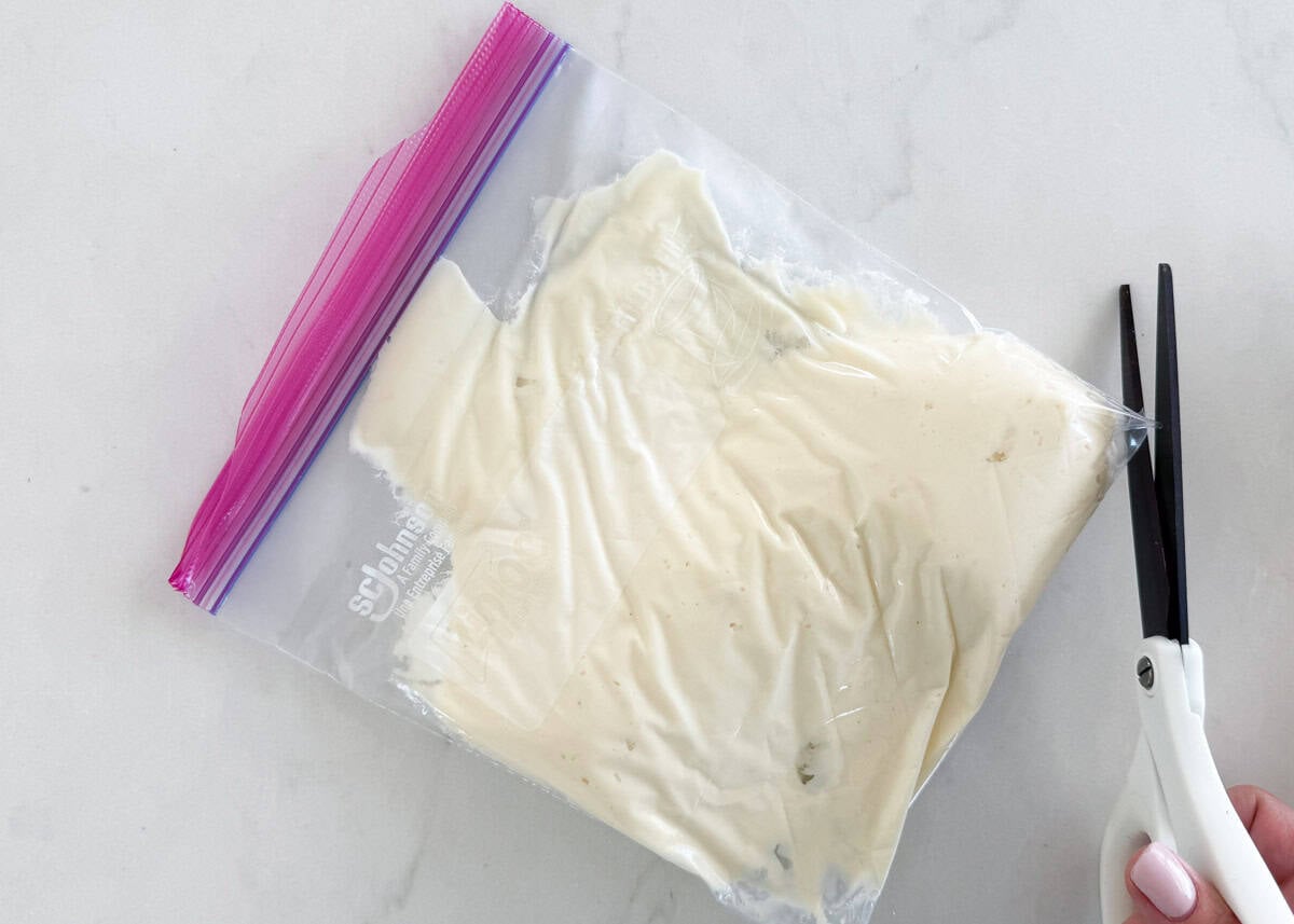 Snipping the corner of a zip-top bag filled with cheesecake filling