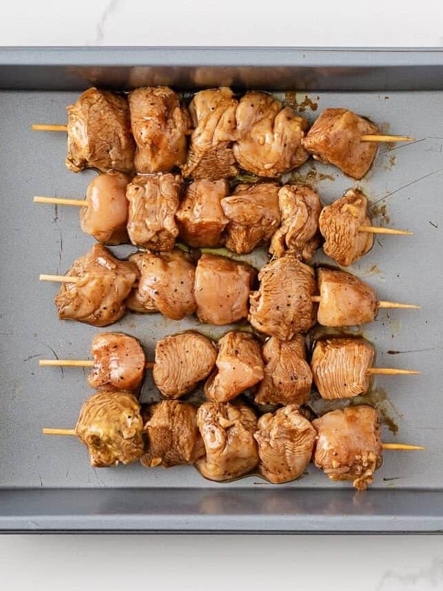 Raw chicken skewers in a pan.
