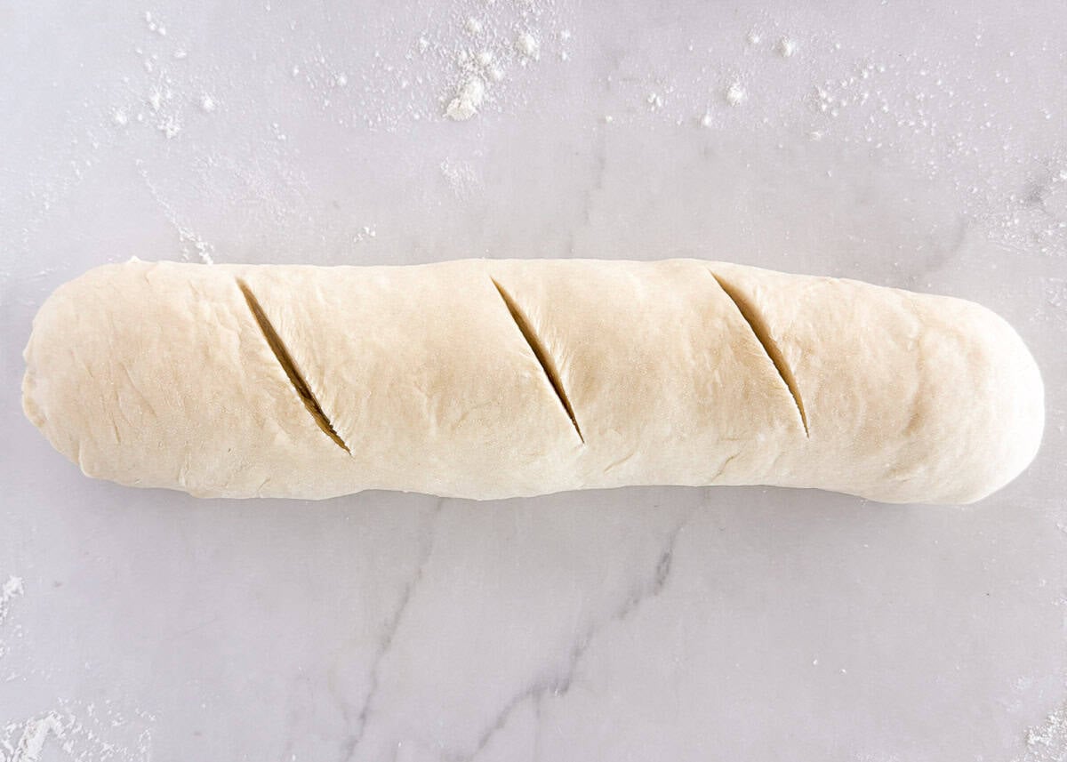 Homemade Italian bread dough shaped into a loaf and scored with diagonal slashes.