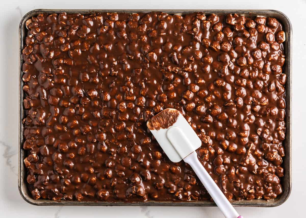 Spreading cooked chocolate icing on top of a sheet cake topped with marshmallows.