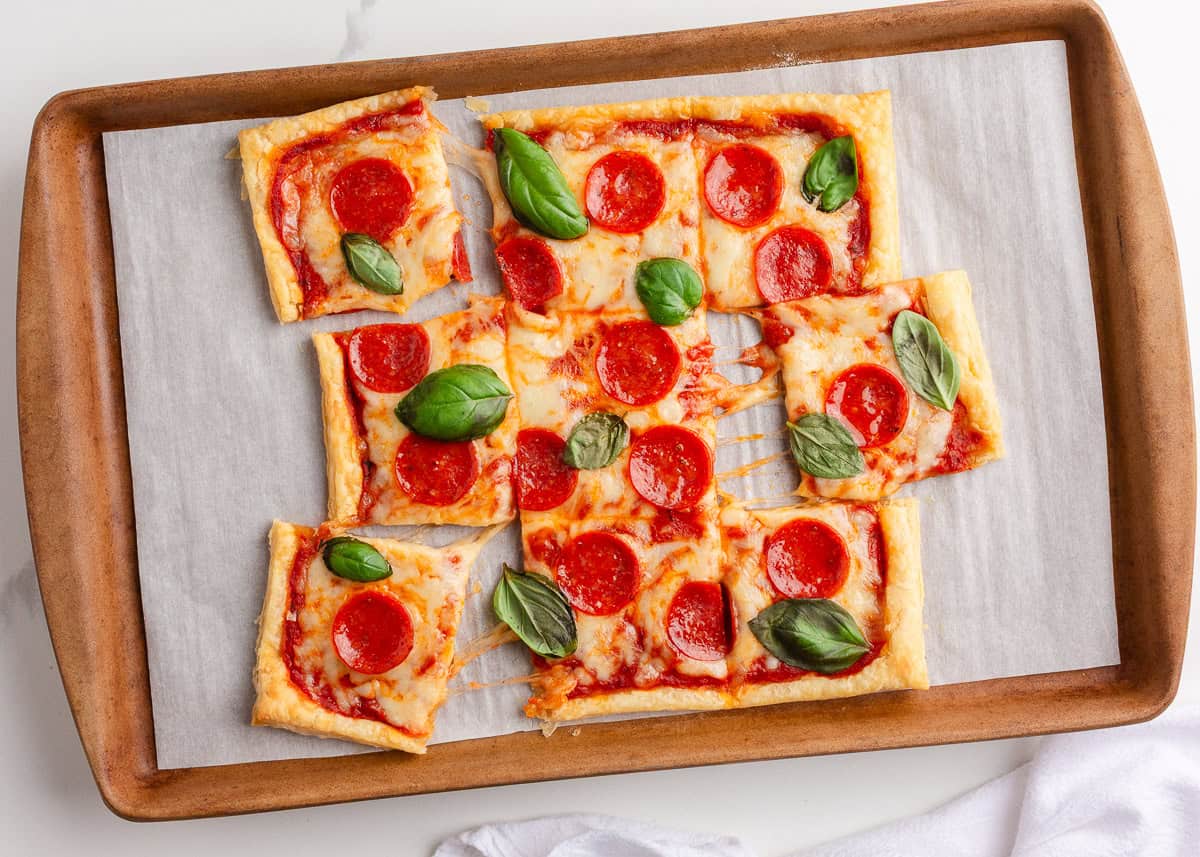 Puff pastry pizza cut into pieces on a baking sheet.