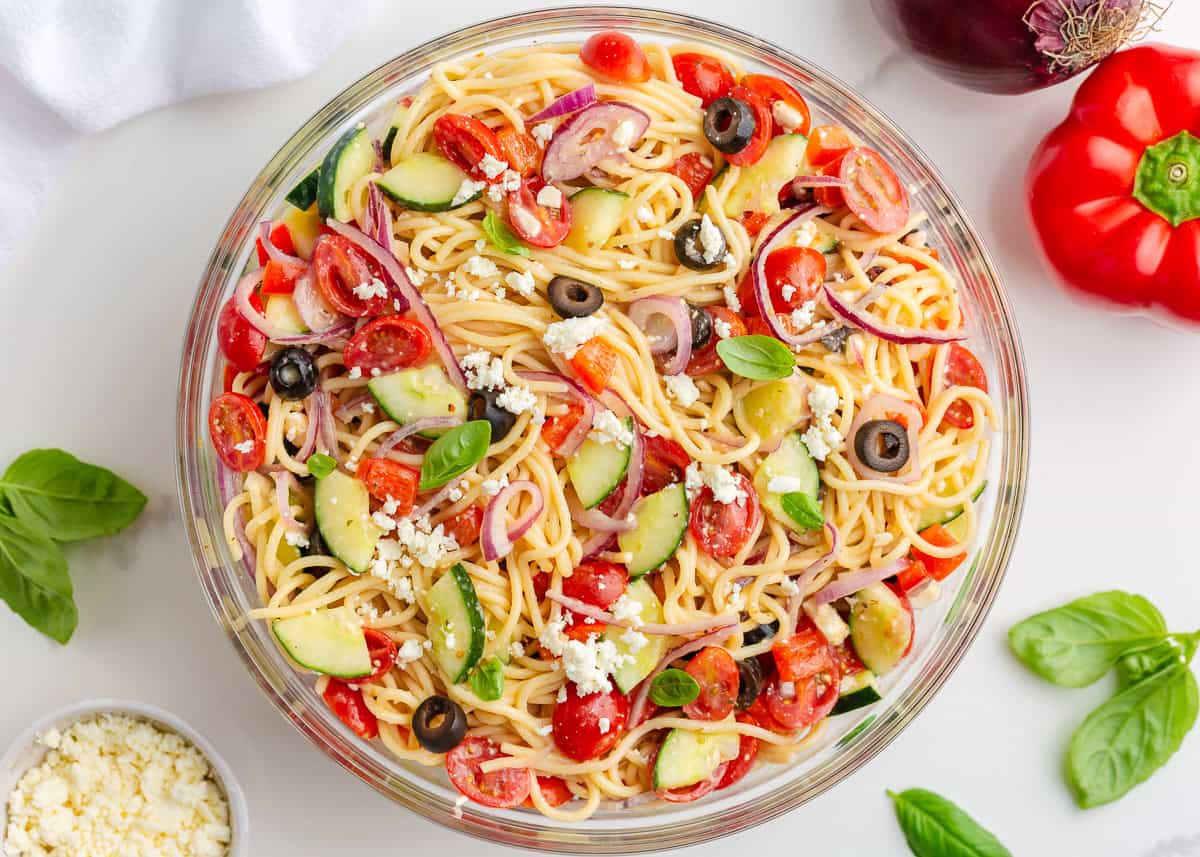 Cold spaghetti salad in a bowl with fresh veggies and tender noodles coated in zesty Italian dressing.