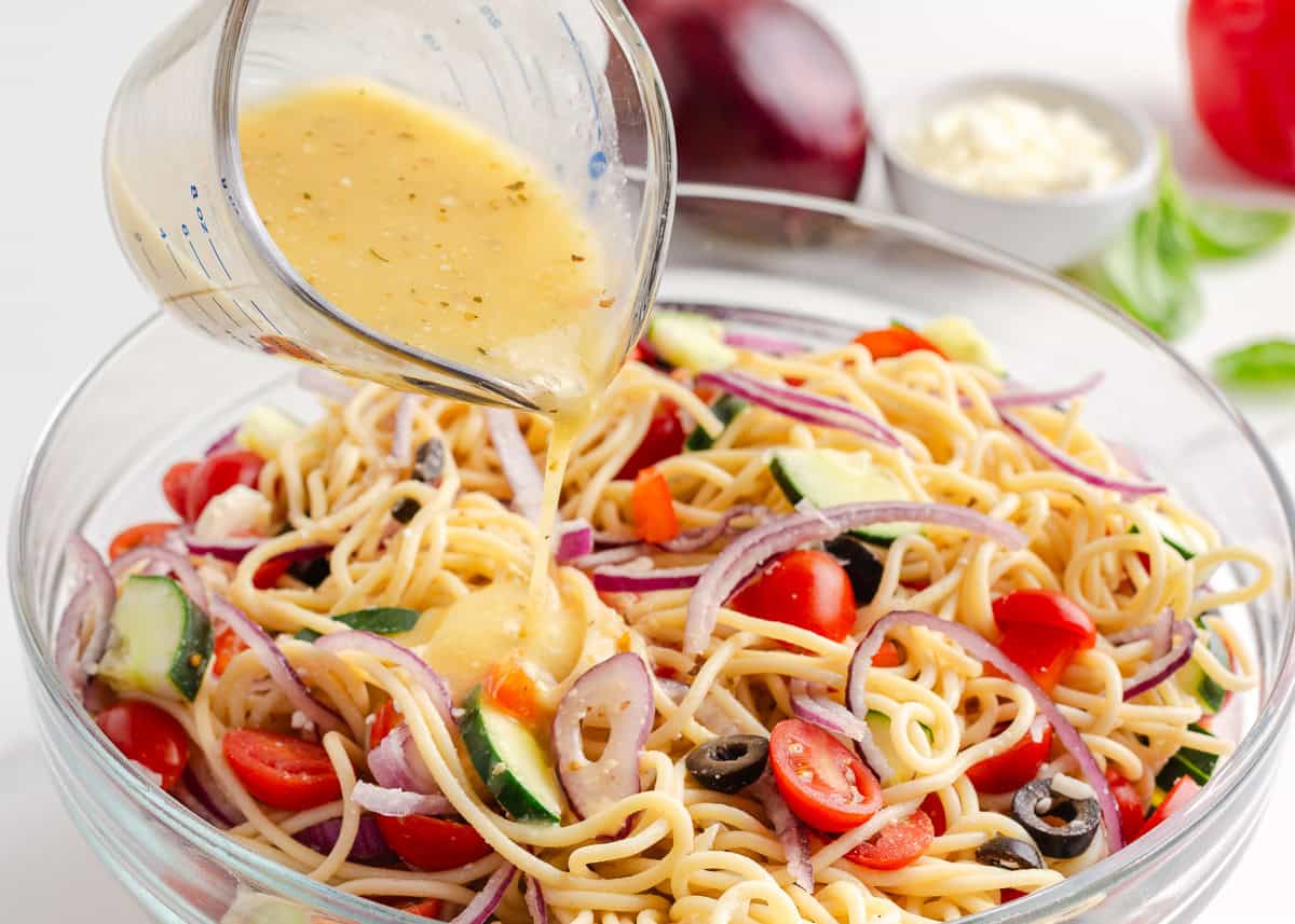 Pouring Italian dressing into a bowl of spaghetti salad.