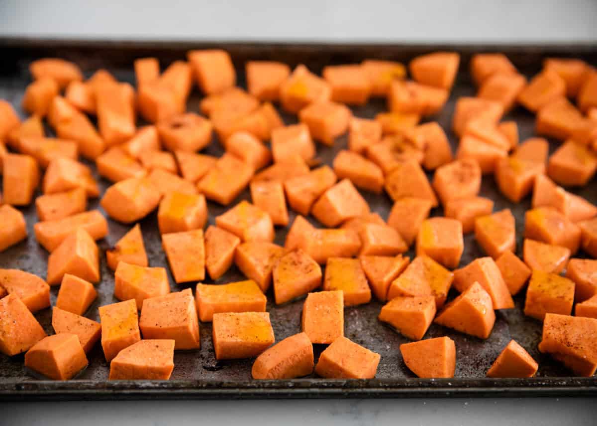Diced sweet potatoes tossed with oil and spices on a baking sheet before roasting.