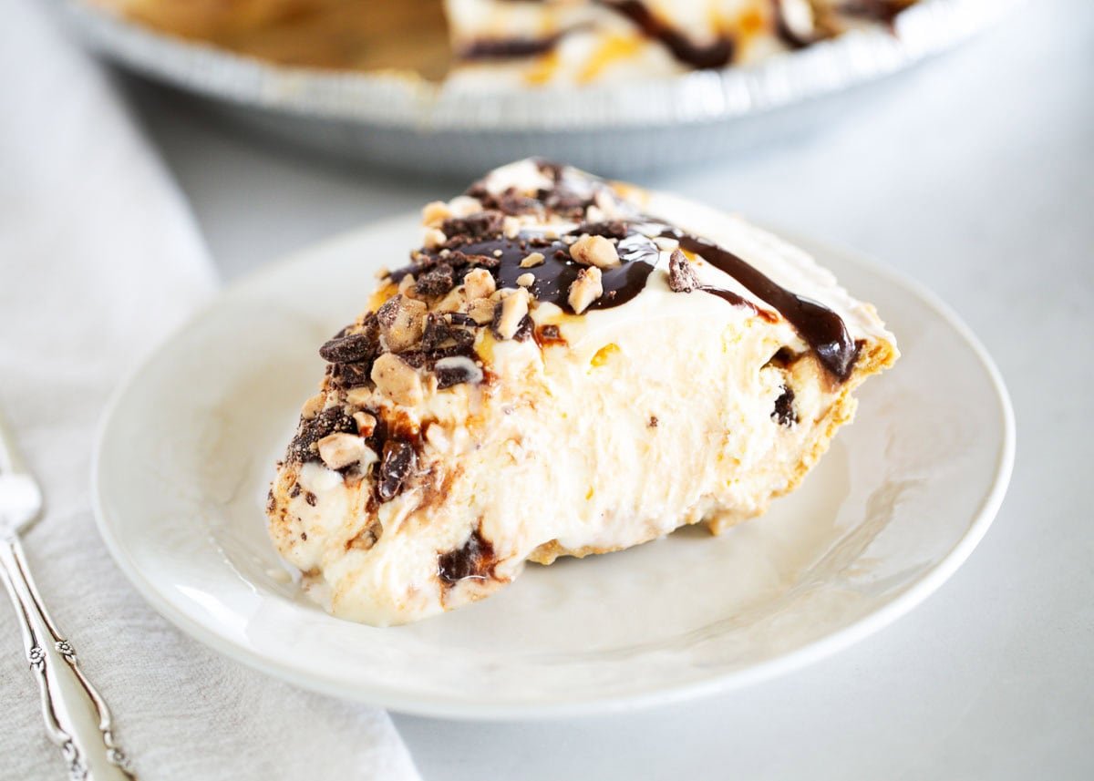 This easy ice cream pie layers vanilla ice cream in a graham cracker crust with hot fudge, caramel, and toffee bits. A no-bake summer dessert favorite with only 5 ingredients! Slice of ice cream pie with caramel, fudge, and toffee on a white plate.