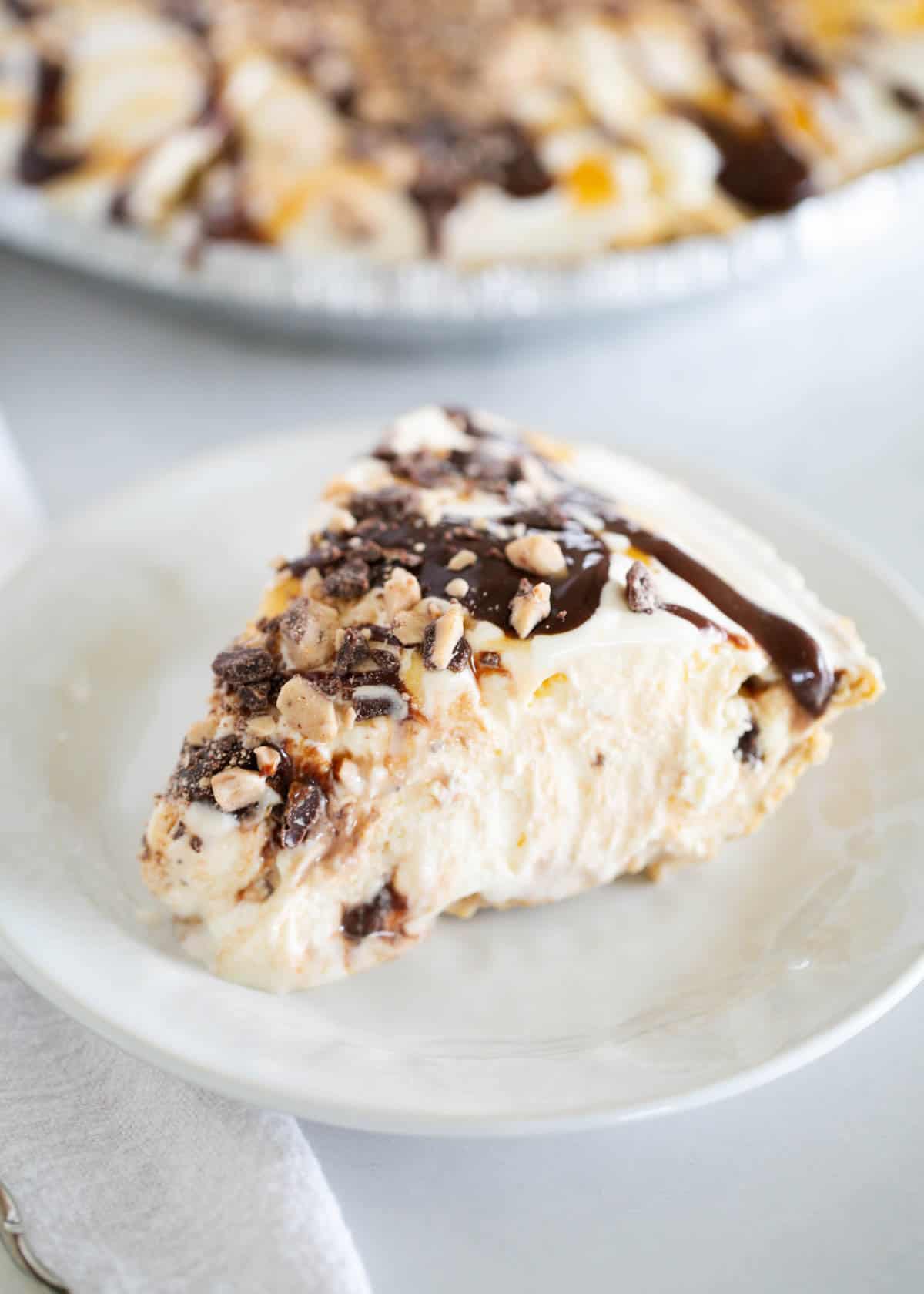 This easy ice cream pie layers vanilla ice cream in a graham cracker crust with hot fudge, caramel, and toffee bits. A no-bake summer dessert favorite with only 5 ingredients! Close-up of a slice of ice cream pie on a plate with gooey toppings.