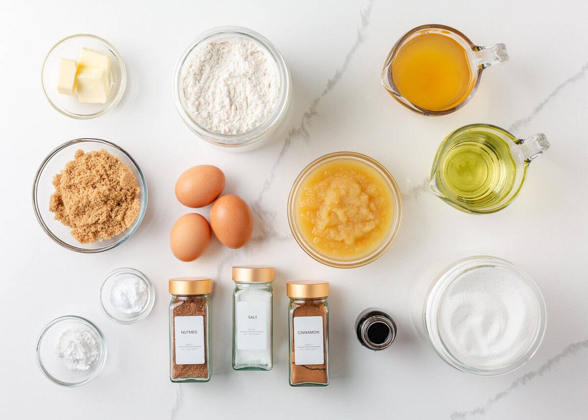 A flat lay of ingredients for apple cider donut cake including applesauce, apple cider, cinnamon and brown sugar.