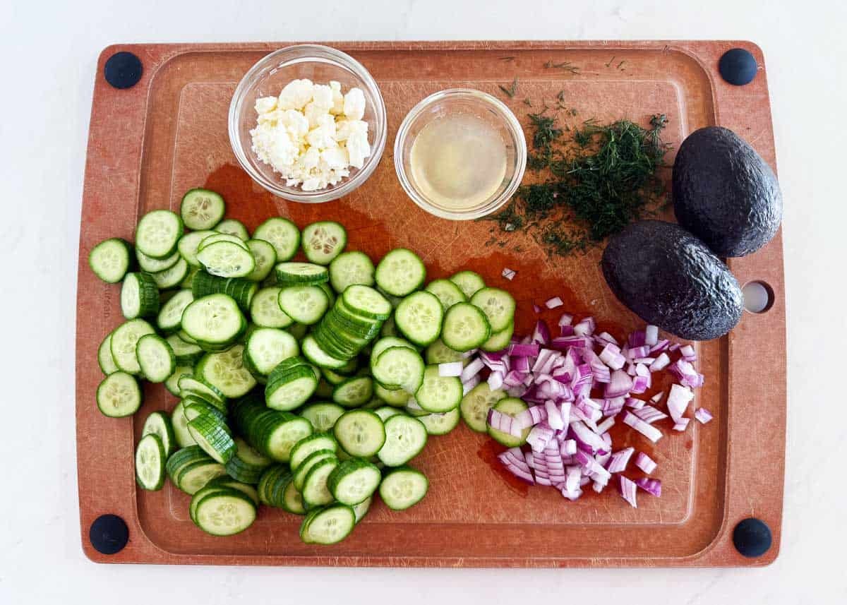 Cucumber avocado salad ingredients on cutting board.