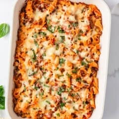 Baked lasagna casserole in a white Staub baking dish topped with melted cheese and fresh basil.
