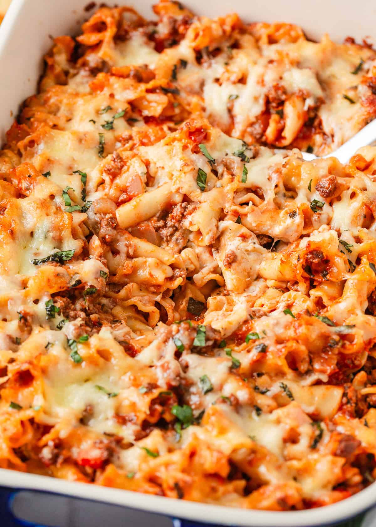 Close-up of lasagna casserole with a serving spoon showing pasta, ground beef, marinara sauce, and melted mozzarella.