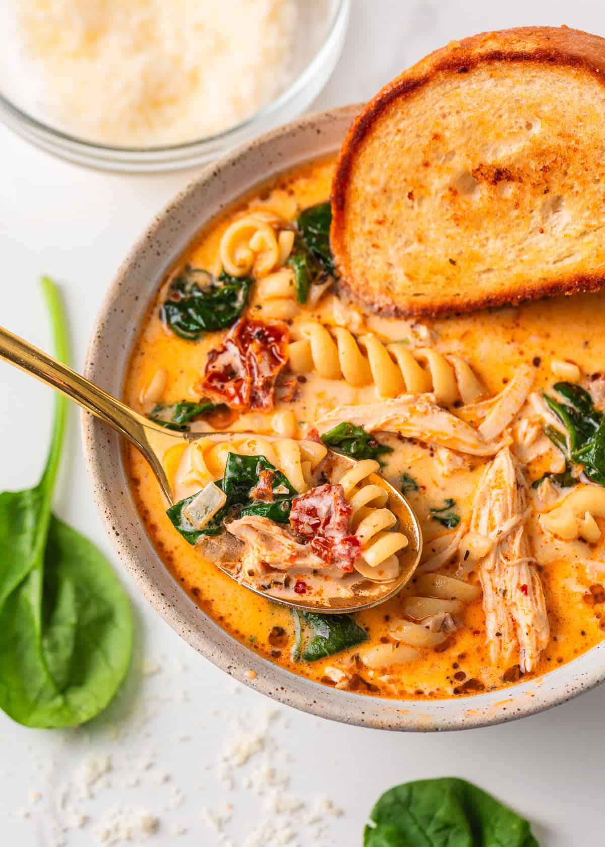 Marry me chicken soup is a cozy spin on the viral marry me chicken recipe made with tender chicken, pasta, sun-dried tomatoes and spinach in a Parmesan cream broth. Bowl of creamy Marry Me Chicken Soup served with a slice of toasted bread and a spoonful of pasta, chicken, and spinach.