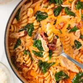 Spoonful of creamy Marry Me Chicken Soup lifted over the pot, showing tender chicken, pasta spirals, sun-dried tomatoes, and wilted spinach.