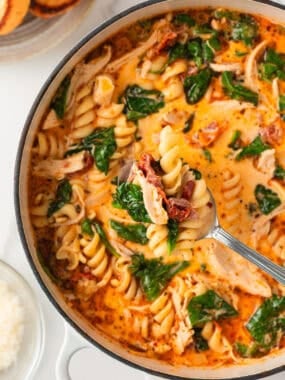 Spoonful of creamy Marry Me Chicken Soup lifted over the pot, showing tender chicken, pasta spirals, sun-dried tomatoes, and wilted spinach.