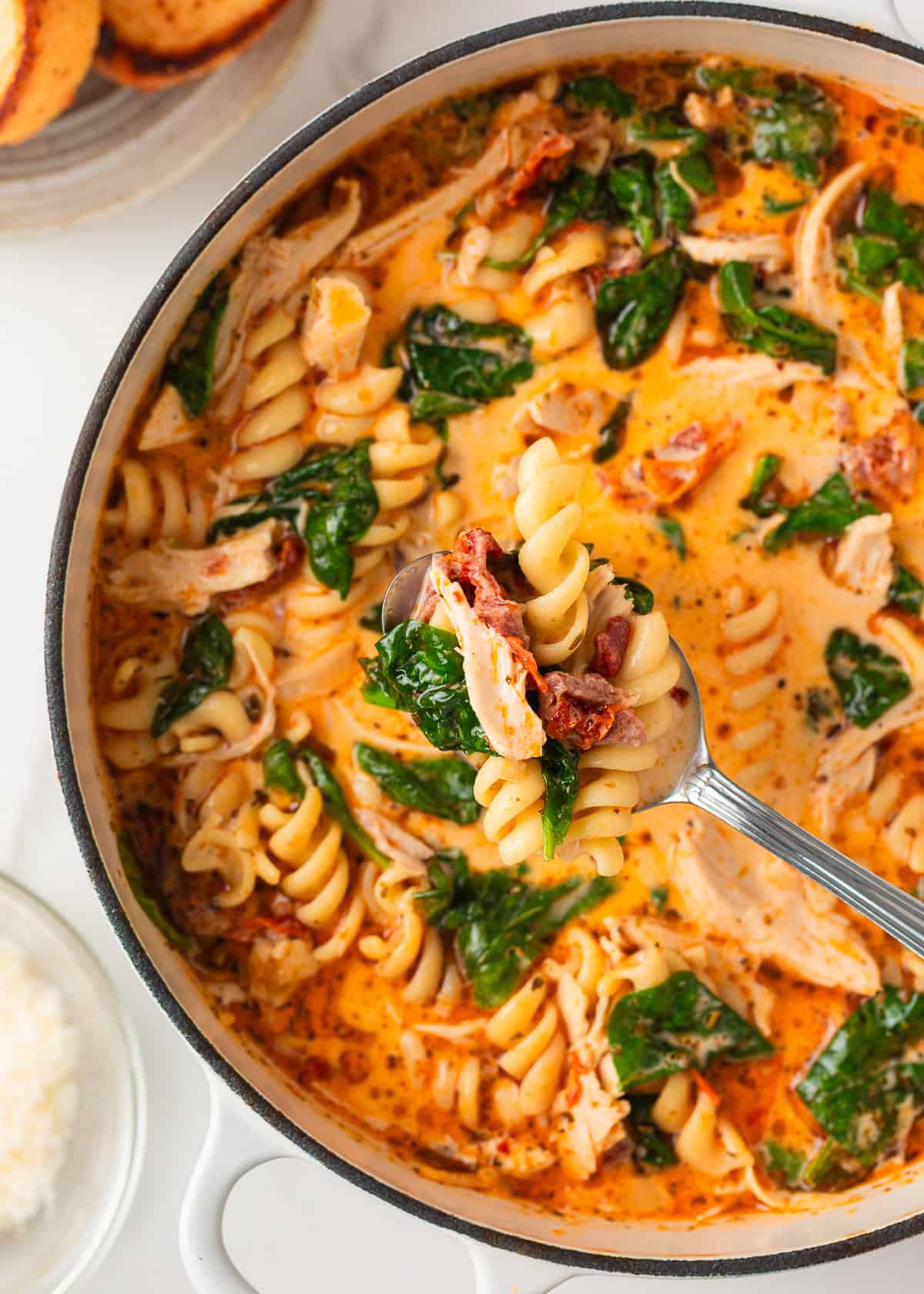 Spoonful of creamy Marry Me Chicken Soup lifted over the pot, showing tender chicken, pasta spirals, sun-dried tomatoes, and wilted spinach.