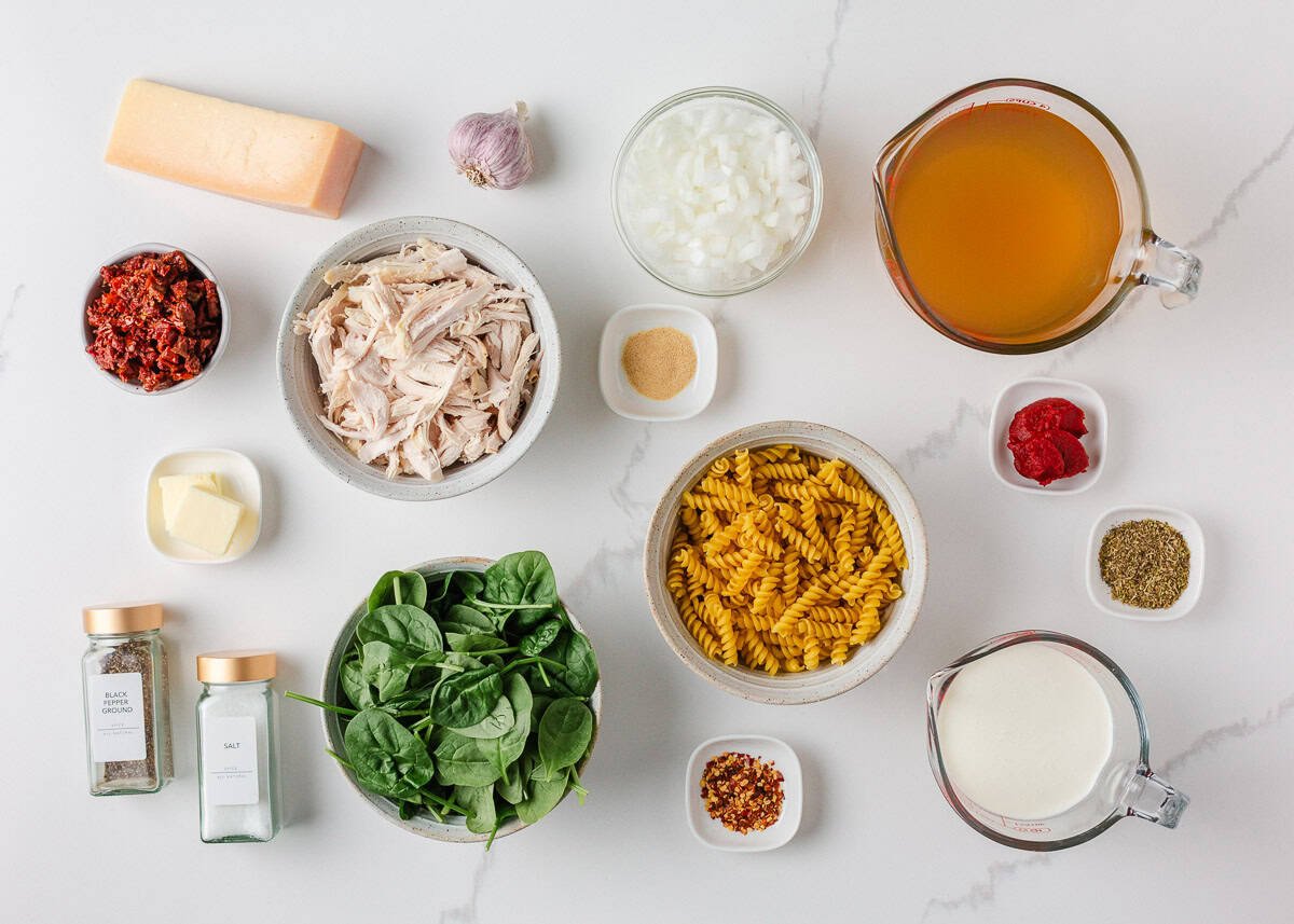Marry me chicken soup is a cozy spin on the viral marry me chicken recipe made with tender chicken, pasta, sun-dried tomatoes and spinach in a Parmesan cream broth. Overhead view of ingredients for marry me chicken soup, including pasta, chicken, spinach, sun-dried tomatoes, onion, garlic, broth, heavy cream, and spices.