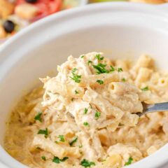 Spoonful of creamy crockpot Olive Garden chicken pasta held over slow cooker with salad in background.