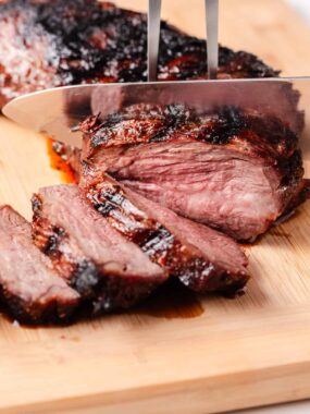 Tri tip being cut on a cutting board.