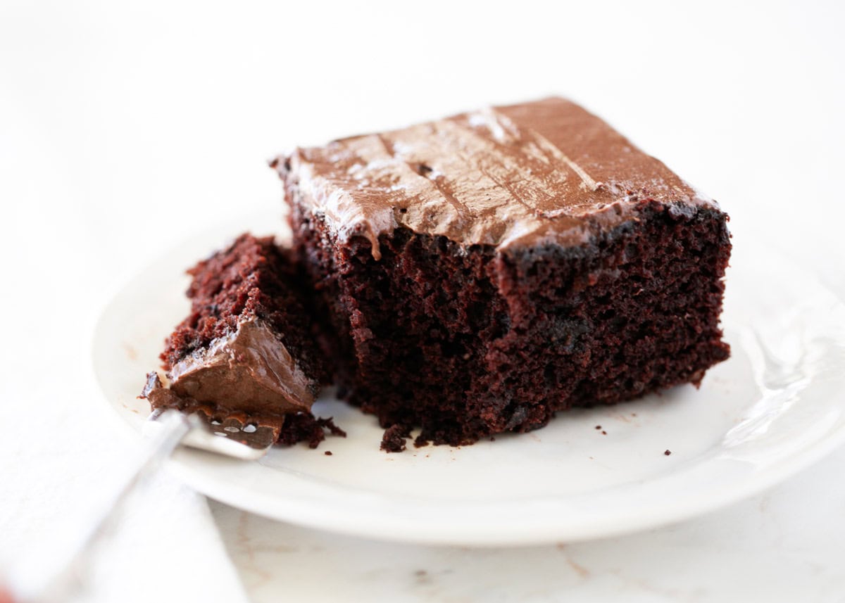 Rich, chocolatey, and moist even without milk, butter, and eggs! This timeless crazy cake originated in a time of scarcity, but is still the perfect way to indulge in a sweet treat! Crazy cake with chocolate frosting on a plate.