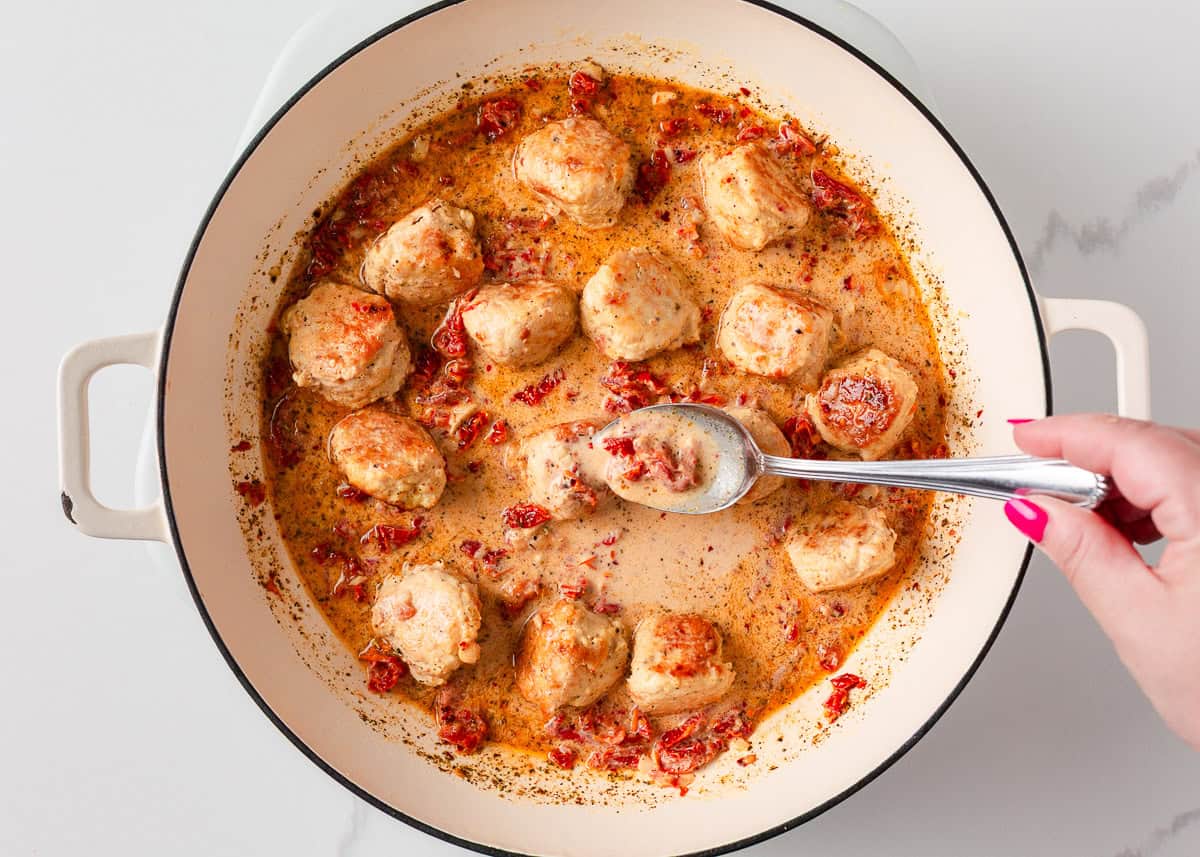 Showing how to spoon the sun dried tomato cream sauce over chicken meatballs.
