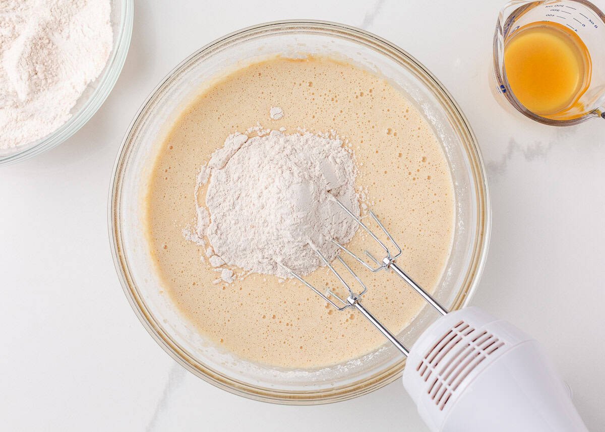 A bowl with wet ingredients showing a mixer adding dry ingredients.
