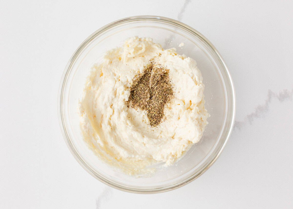 Ricotta cheese mixture with Italian herbs in a glass bowl for layering in easy lasagna casserole.

