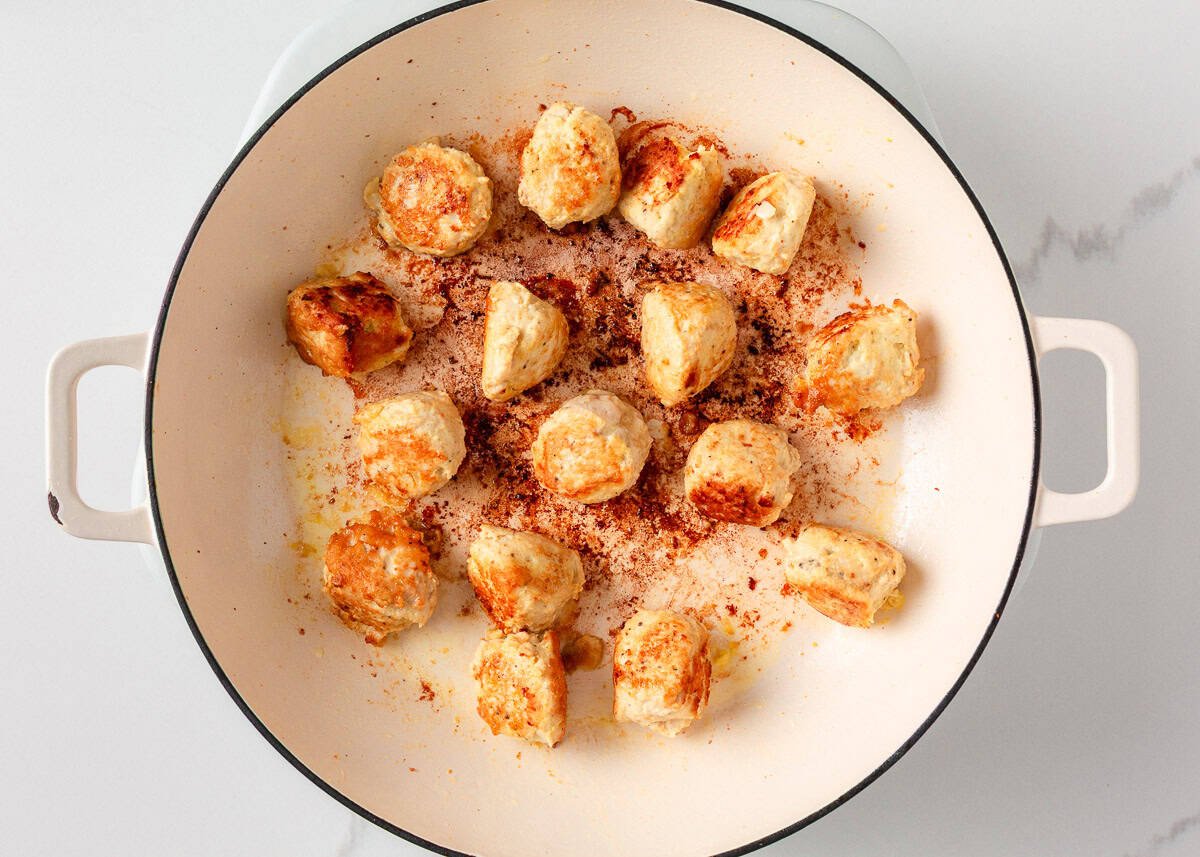 Chicken meatballs pan frying in pan.