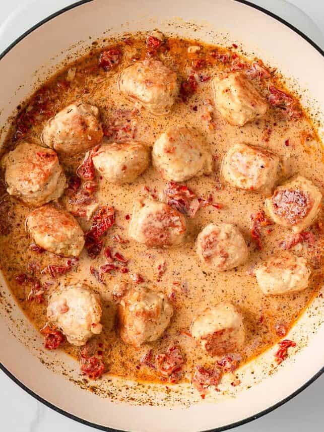 Sun dried tomato cream sauce with chicken meatballs in a pan.