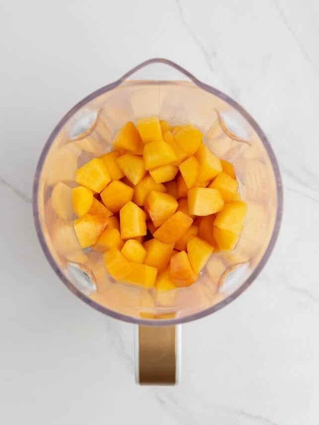 Chopped peaches in a blender, ready to be pureed for peach freezer jam.