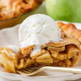 Slice of favorite apple pie on a plate topped with a scoop of vanilla ice cream, showcasing the flaky crust and cinnamon apple layers.
