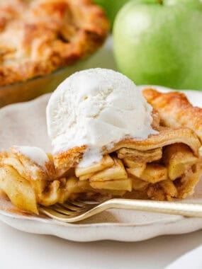 Slice of favorite apple pie on a plate topped with a scoop of vanilla ice cream, showcasing the flaky crust and cinnamon apple layers.