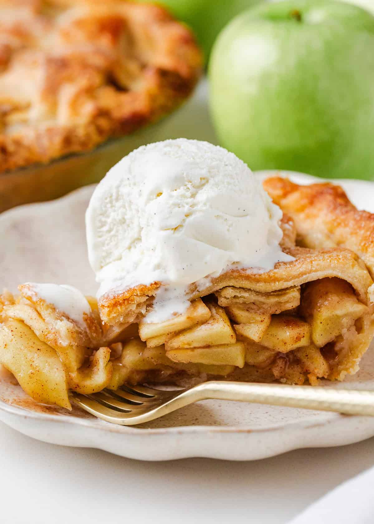 Slice of favorite apple pie on a plate topped with a scoop of vanilla ice cream, showcasing the flaky crust and cinnamon apple layers.