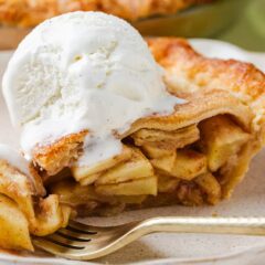 Close-up of a slice of apple pie with melty vanilla ice cream on top, fork cutting into the soft cinnamon-spiced apple filling.