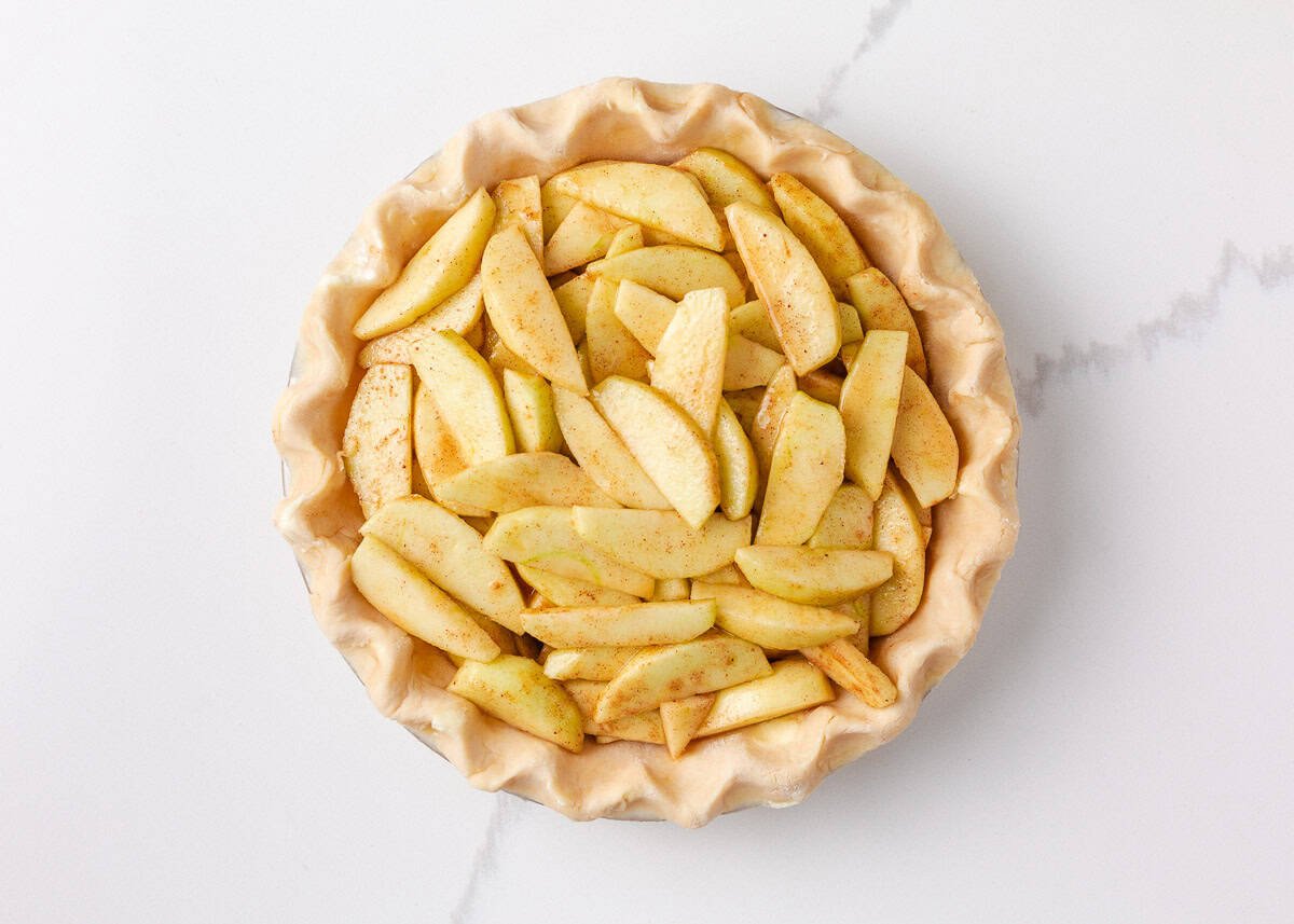 Unbaked pie crust filled with spiced apple slices, ready to be topped with the upper crust.