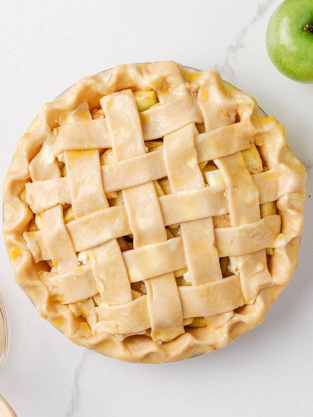 Apple pie topped with an unbaked lattice crust and crimped edges, ready for the egg wash and baking.