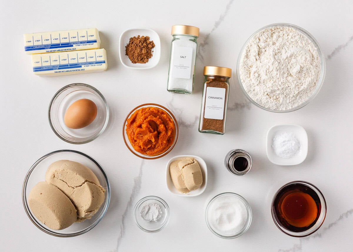 Perfectly spiced and deliciously sweet with the nutty aroma of brown butter, these chewy brown butter pumpkin cookies deliver all the fall coziness in every bite! Overhead image of brown butter pumpkin cookie ingredients, including pumpkin purée, brown sugar, flour, spices, egg, and vanilla on a white marble counter.