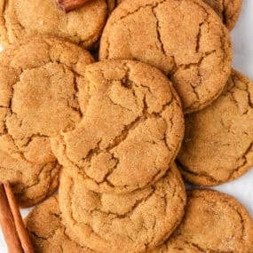 Overhead shot of chewy brown butter pumpkin cookies with warm cracks and a bite taken out, surrounded by whole cookies and cinnamon sticks.