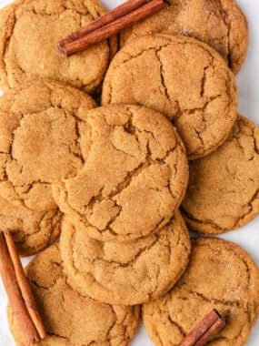 Overhead shot of chewy brown butter pumpkin cookies with warm cracks and a bite taken out, surrounded by whole cookies and cinnamon sticks.