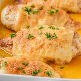 Close-up of baked Swiss chicken in casserole dish with melted cheese and garnished with parsley.