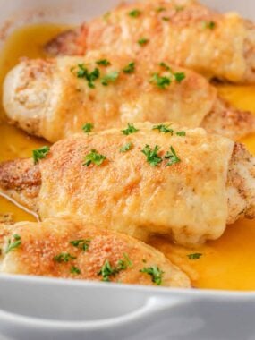 Close-up of baked Swiss chicken in casserole dish with melted cheese and garnished with parsley.
