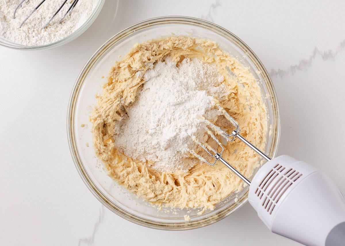 Softened butter and sugar mixture in a bowl with cake flour being mixed in using a hand mixer.