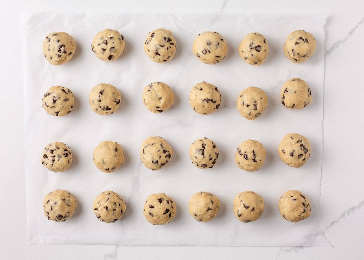 Uniform rows chocolate chip cookie dough balls lined up on parchment paper, ready for chilling.