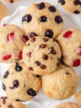 Overhead view of assorted pancake muffins made with pancake mix topped with chocolate chips, blueberries, and strawberries arranged in a circle on a white platter.