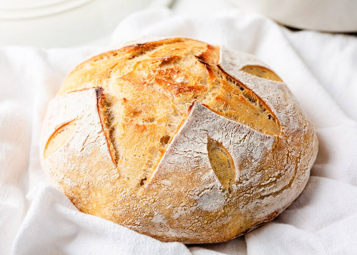 With no overnight rise required, same day sourdough bread is the perfect way for any beginner or expert baker to bake up a fresh, homemade loaf in just 8 hours! Golden brown round loaf of same day sourdough bread with decorative scoring, placed on a soft white kitchen towel.