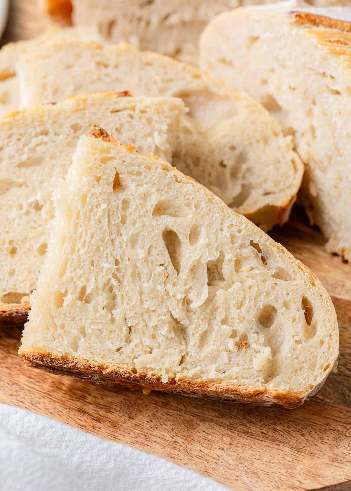 Slices of same day sourdough bread fanned out on a wooden board, highlighting the open crumb structure and crisp crust.